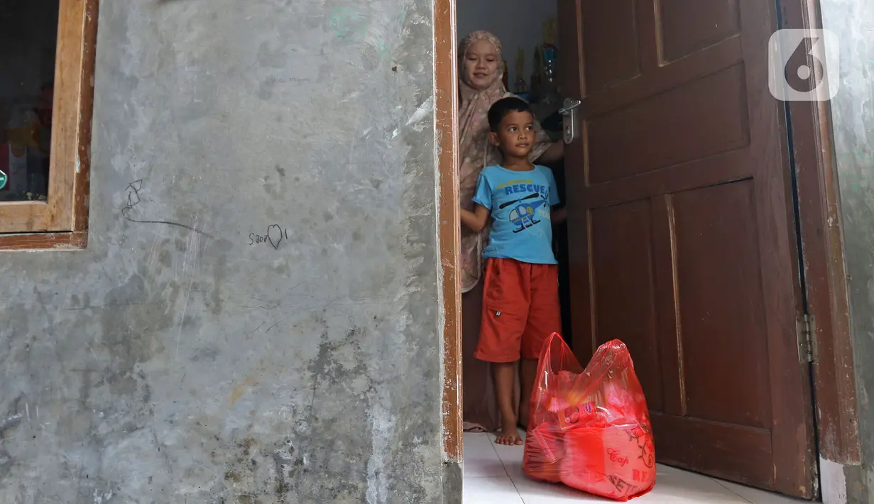 Warga menerima bantuan bahan pokok di rumahnya di RT03/RW03, Kelurahan Cilangkap, Jakarta, Jumat (21/5/2021). Sebanyak 25 paket bahan pokok dari bantuan Dinas Sosial DKI Jakarta dan swadaya warga setempat diberikan kepada 25 Kepala Keluarga. (Liputan6.com/Herman Zakharia)