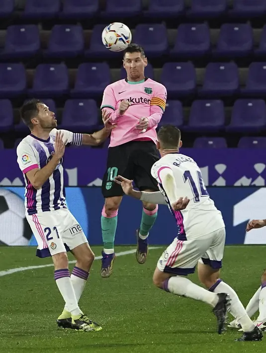 Penyerang Barcelona, Lionel Messi melompat saat berebut bola dengan pemain Valladolid pada laga pekan ke-15 Liga Spanyol di Stadion Jose Zorrilla, Selasa (22/12/2020). Messi resmi melewati rekor Pele saat membantu Barcelona menggulung Valladolid 3-0 dalam laga tersebut. (Cesar Manso/Pool via AP)
