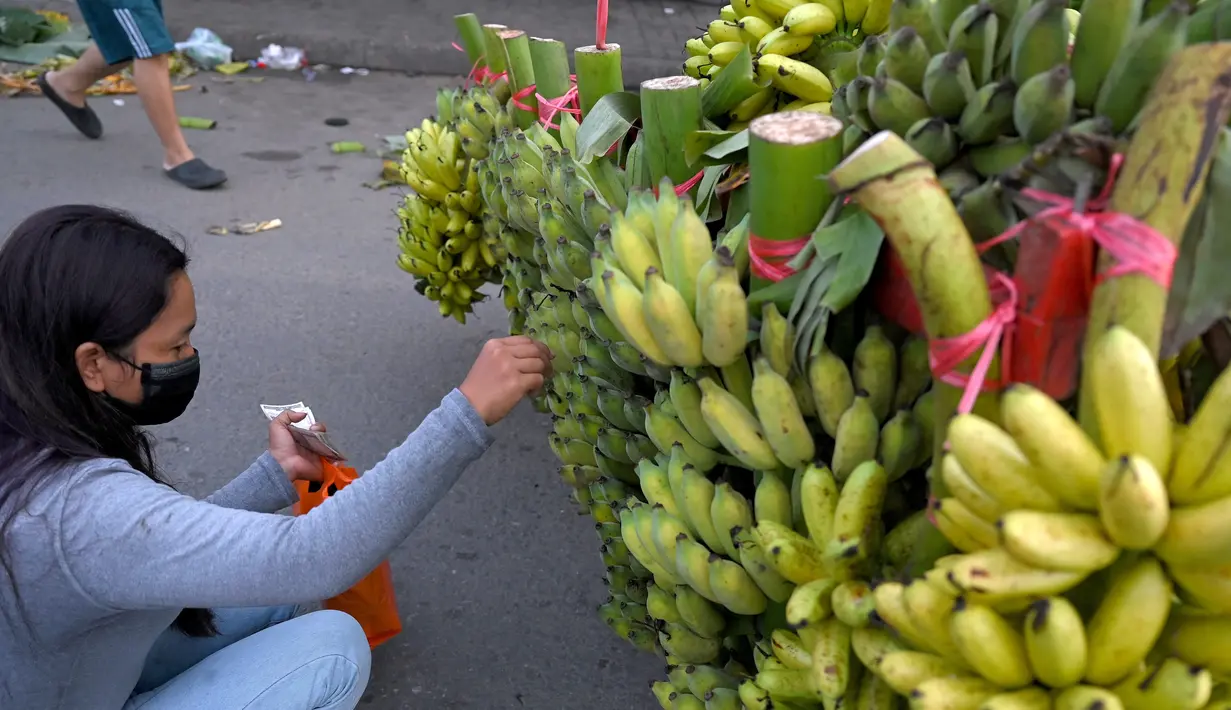 Seorang wanita membeli pisang di sepanjang jalan di Phnom Penh (13/10/2021). Tiga spesies pisang  kuning, gula dan hijau semuanya banyak ditanam di Kamboja. (AFP/Tang Chhin Sothy)