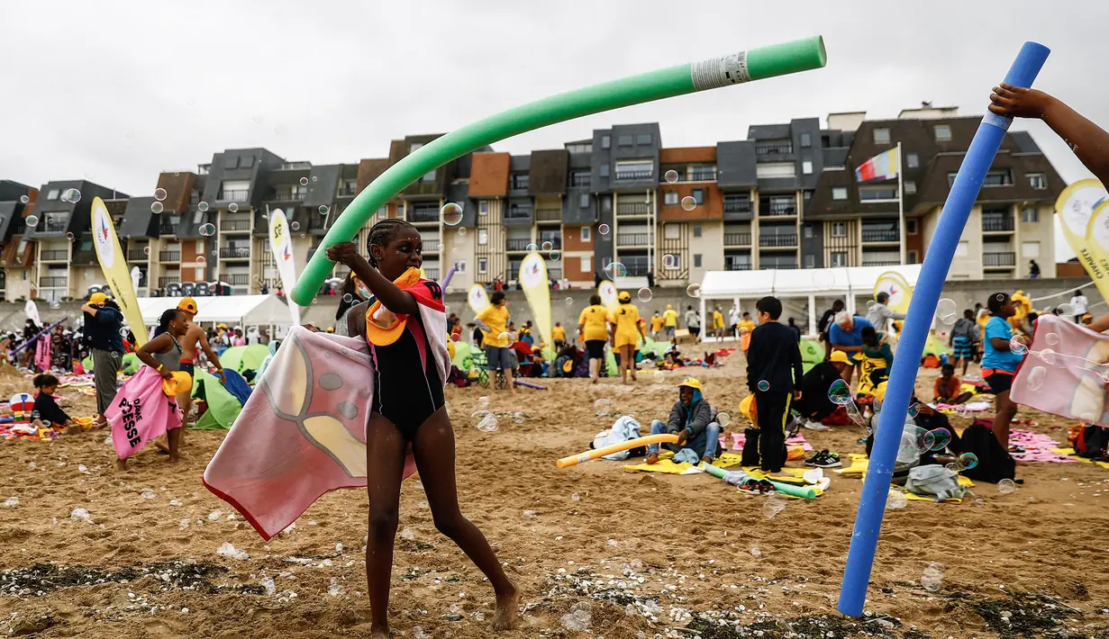 Anak-anak bermain dengan gelembung di pantai Cabourg, barat laut Prancis (18/8/2021). Seratus bus meninggalkan wilayah Paris dari delapan departemen Ile-de-France dengan 5.000 anak muda dari Ile-de-France dalam situasi genting yang belum sempat berangkat musim panas ini. (AFP/Sameer Al-Doumy)