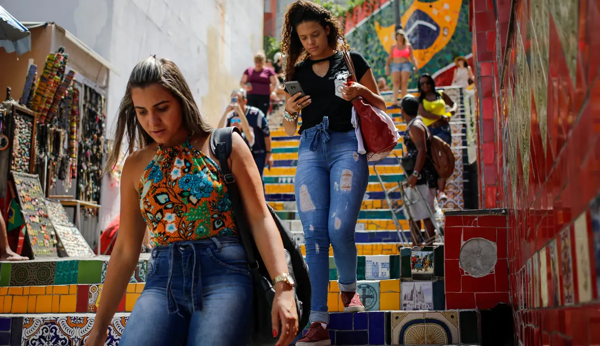 Pejalan kaki melintasi anak tangga yang terkenal dengan nama Selaron Steps atau Escadaria Selarón di Rio de Janeiro, Brasil pada 9 Desember 2019. Sang seniman pembuat yang bernama Jorge Selaron mempersembahkan karya seninya untuk rakyat Brasil. (Photo by David GANNON / AFP)
