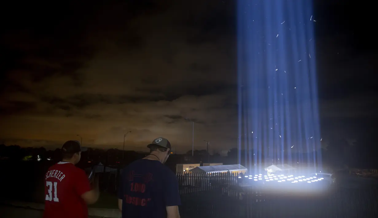 Orang-orang melihat pertunjukan cahaya saat mengunjungi penghormatan ringan untuk serangan 9/11 di Pentagon di Arlington, Virginia (10/9/2020). Pertunjukan tersebut adalah bagian dari peringatan skala kecil tahun ini karena pandemi virus corona. (Tasos Katopodis / Getty Images / AFP)