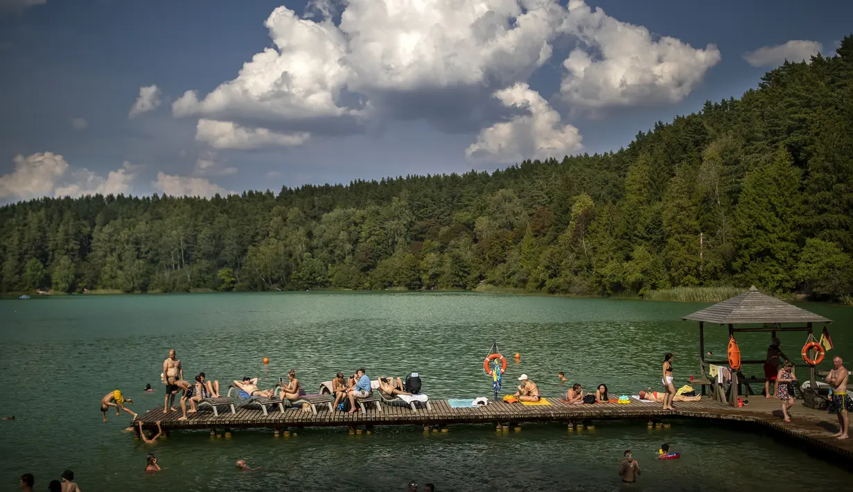 Orang-orang menikmati cuaca hangat di tepi danau dekat Vilnius, Lituania, Kamis, 17 Agustus 2023.(AP Photo/Mindaugas Kulbis)