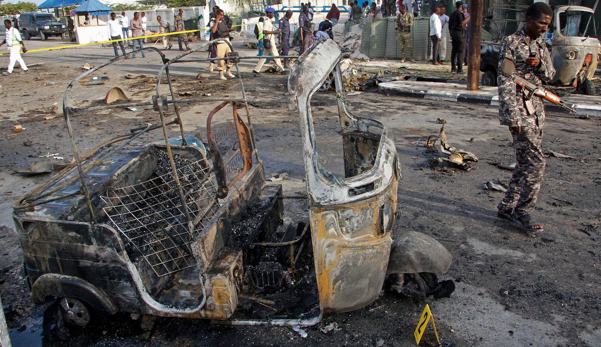 Tentara Somalia melewati puing kendaraan di lokasi ledakan bom mobil dekat pos pemeriksaan parlemen dan Kementerian Dalam Negeri di Mogadishu, Minggu (25/3). Ledakan terjadi di kawasan yang dijaga dengan sangat ketat di kota itu. (AP/Farah Abdi Warsameh)