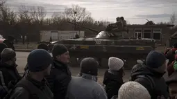 Warga yang mengantre bantuan menyaksikan tentara Ukraina menaiki tank di kota Trostsyanets, Ukraina, Senin, 28 Maret 2022. Trostsyanets baru-baru ini direbut kembali oleh pasukan Ukraina setelah dikuasai oleh Rusia sejak awal perang. (AP Photo/Felipe Dana)