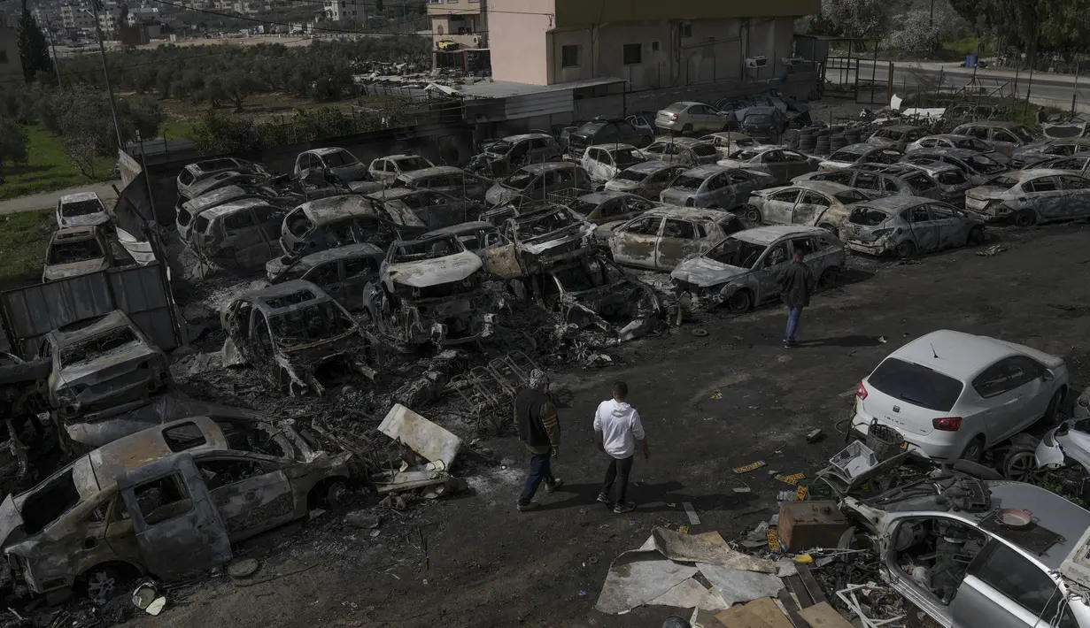 Warga Palestina berjalan di samping mobil yang hangus di tempat pembuangan sampah, di kota Hawara, dekat kota Nablus di Tepi Barat, Senin, 27 Februari 2023. Petugas medis Palestina mengatakan satu orang tewas dan empat lainnya terluka parah dalam apa yang tampaknya ledakan kekerasan pemukim terburuk dalam puluhan tahun. (AP Photo/Nasser Nasser)