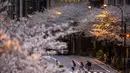 Orang-orang yang mengenakan masker pelindung untuk membantu mengekang penyebaran virus corona berjalan melintasi jalan di bawah bunga sakura di Tokyo, Minggu (28/3/2021). (AP Photo/Kiichiro Sato)