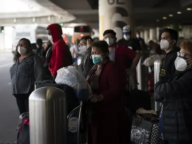 Pelancong menunggu bus antar-jemput tiba di Bandara Internasional Los Angeles di Los Angeles, Senin (20/12/2021). Departemen Kesehatan Masyarakat Los Angeles County melaporkan lebih dari 3.500 kasus baru COVID-19 pada hari Minggu. (AP Photo/Jae C.Hong)
