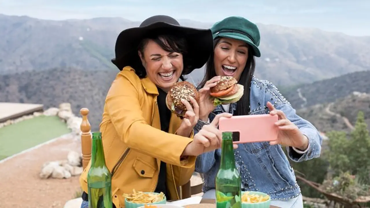 Dua orang perempuan sedang mengambil foto sambil menikmati makanan di atas pegunungan (Foto Dok: Freepik/freepik)