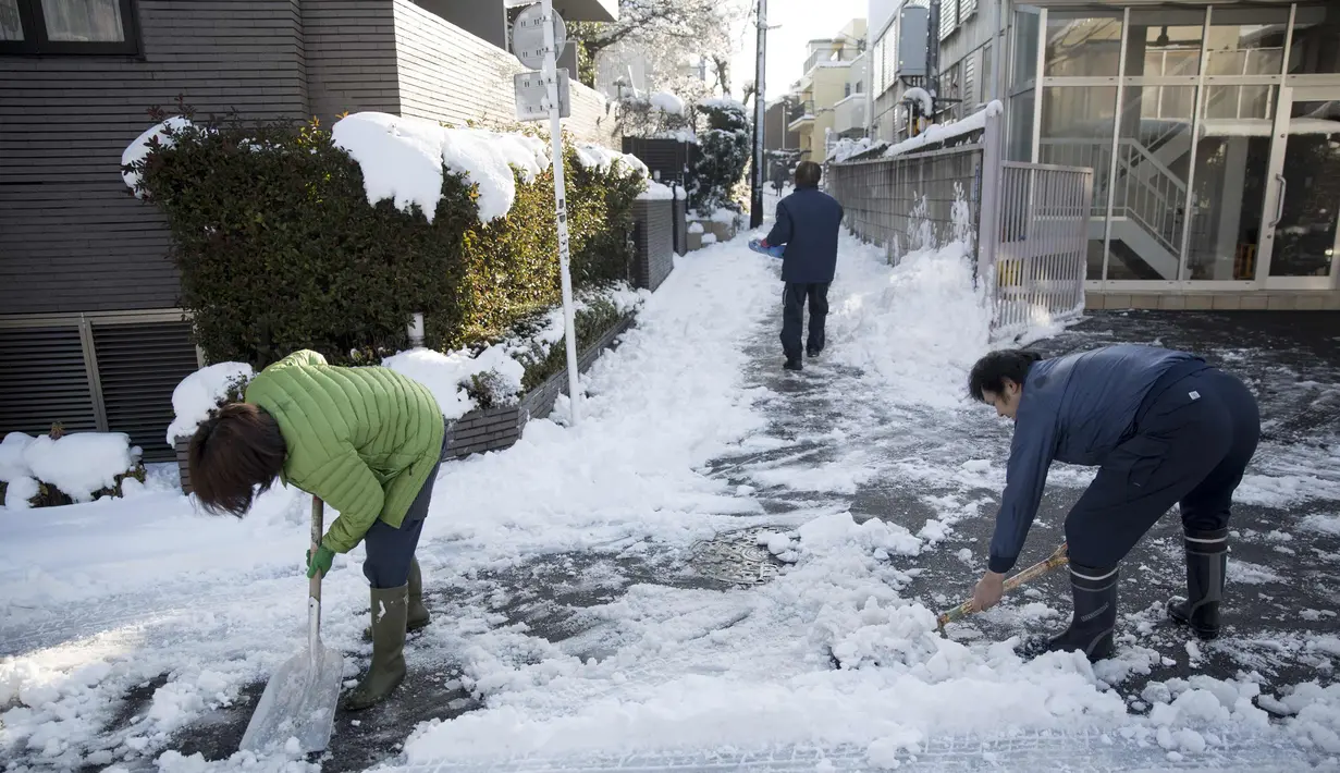 Warga menyingkirkan salju di luar rumah mereka di bangsal Meguro di Tokyo (23/1). Hujan salju membuat keberangkatan penerbangan dan melumpuhkan beberapa layanan kereta api di kota tersebut. (AFP Photo/Behrouz Mehri)