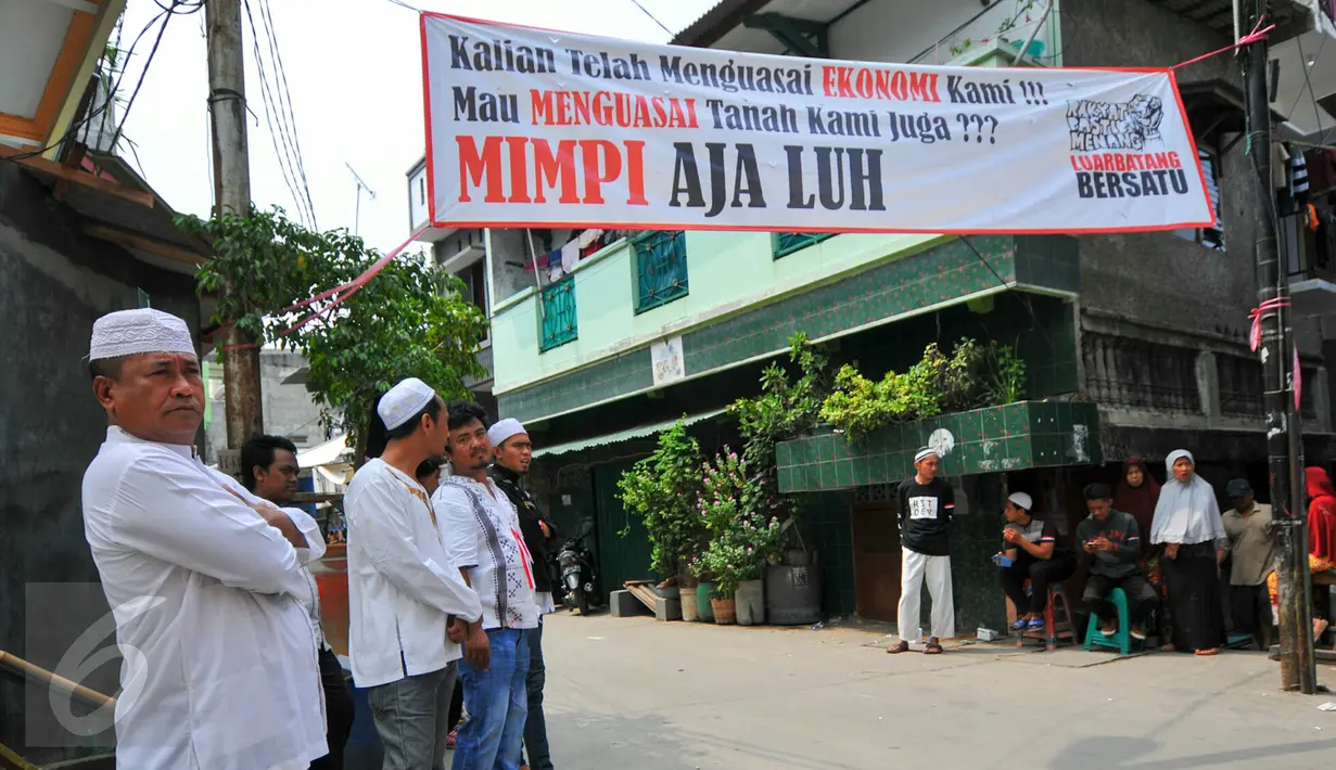 Sejumlah warga berdiri di bawah spanduk penolakan penggusuran Kampung Luar Batang, Penjaringan, Jakarta, Rabu (20/4). Mereka menolak pembongkaran tahap dua yang akan dilakukan Pemprov DKI pada Mei nanti. (Liputan6.com/Yoppy Renato)