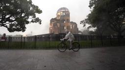 Seorang pengendara sepeda terjebak dalam hujan lebat di dekat Kubah Bom Atom di Hiroshima, Jepang barat, Kamis (15/7/2021). Atomic Bomb Dome atau kubah bom atom yang merupakan bagian dari taman perdamaian Hiroshima. AP Photo/Eugene Hoshiko)