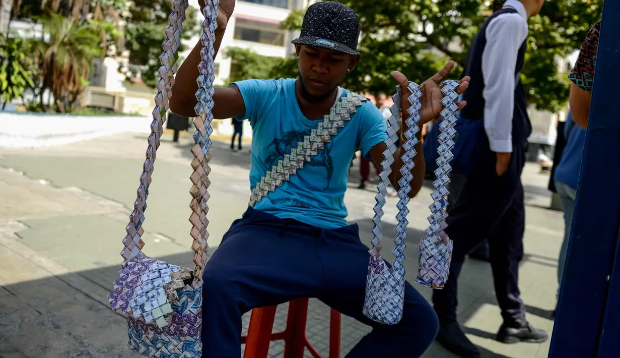 Wilmer Rojas (25) menunjukkan tas dari lembaran mata uang Bolivar di Caracas, Venezuela, 30 Januari 2018. Lembaran uang tersebut kini tidak lagi menjadi alat jual beli, melainkan bahan untuk membuat kerajinan tangan. (AFP Photo/Federico Parra)