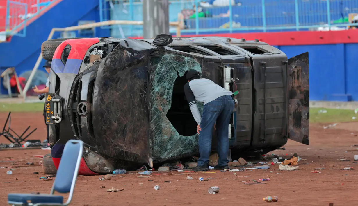 Seorang petugas polisi berpakaian preman memeriksa mobil polisi yang rusak dalam tragedi kerusuhan pada pertandingan sepak bola antara Arema Vs Persebaya di Stadion Kanjuruhan Malang, Jawa Timur, Minggu (2/10/2022). Sejauh ini ada sebanyak 180 orang yang sedang dirawat di beberapa rumah sakit yang tersebar di Malang Raya. (AP Photo/Trisnadi)