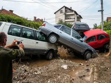 Warga mengambil gambar mobil yang rusak akibat banjir bandang di Ibu Kota Skopje, Makedonia, Minggu (7/8). Pemerintah menyatakan keadaan darurat sehari setelah setidaknya 21 orang tewas dalam banjir bandang yang disebabkan badai. (Robert ATANASOVSKI/AFP)