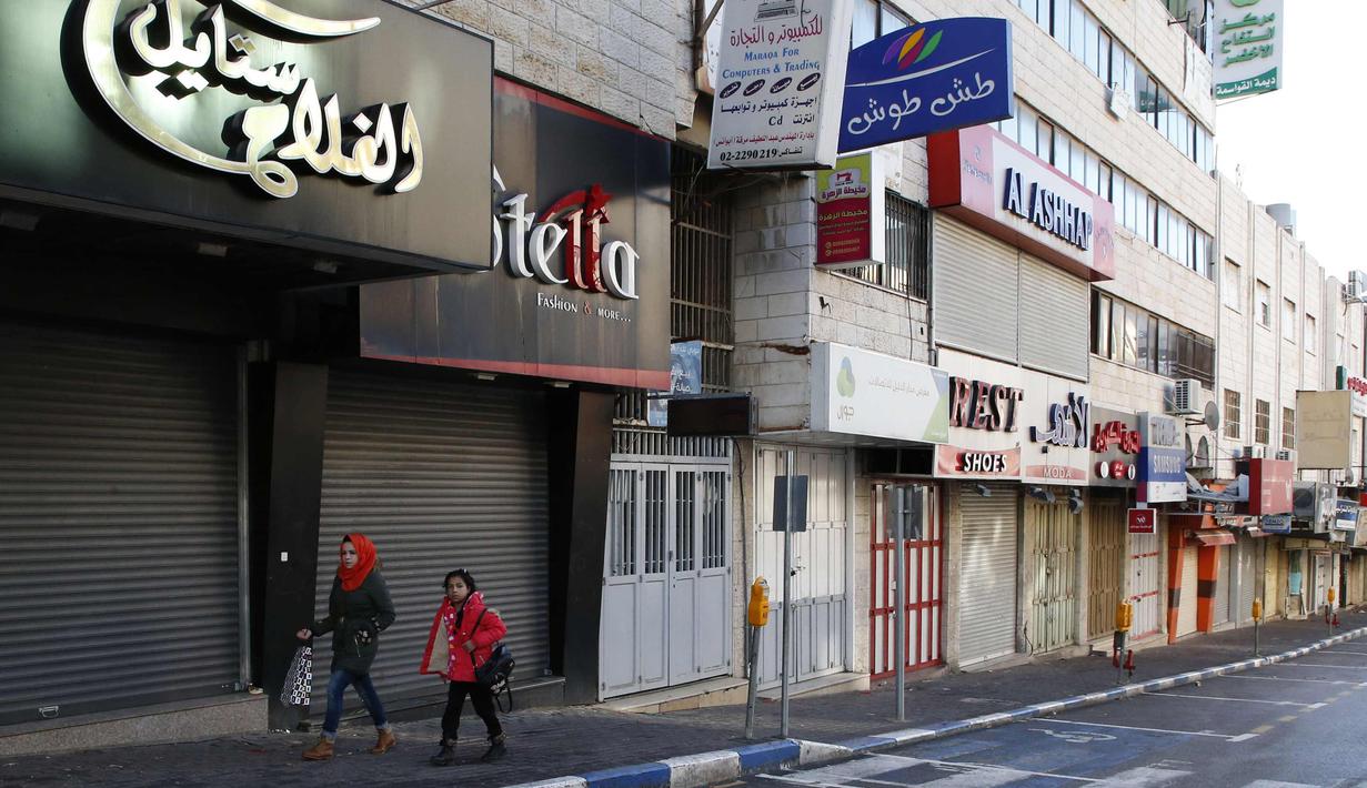 Warga Palestina berjalan melewati toko-toko yang tutup di kota Nablus, Tepi Barat, (7/12). Usai Presiden AS, Donald Trump mengumumkan Yerusalem sebagai ibu kota Israel suasana sepi terlihat di kawasan tersebut. (AFP Photo/Hazem Bader)