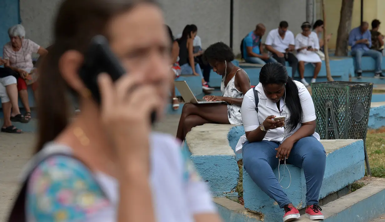 Orang-orang menggunakan ponsel dan laptop untuk terhubung ke internet melalui WiFi di sebuah taman di Havana, Rabu (5/12). Untuk pertama kalinya, masyarakat Kuba berkesempatan dapat mengakses internet dari ponsel mereka pada Kamis ini, (YAMIL LAGE/AFP)