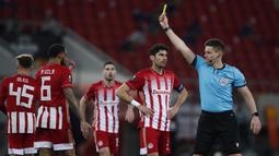 Wasit Daniel Siebert memberikan kartu kuning kepada gelandang Olympiakos, Yann M'Vila (kedua dari kiri) dalam laga leg pertama babak 16 besar Liga Europa 2020/2021 di Georgios Karaiskakis Stadium, Kamis (11/3/2021). Olympiakos kalah 1-3 dari Arsenal. (AP/Thanassis Stavrakis)