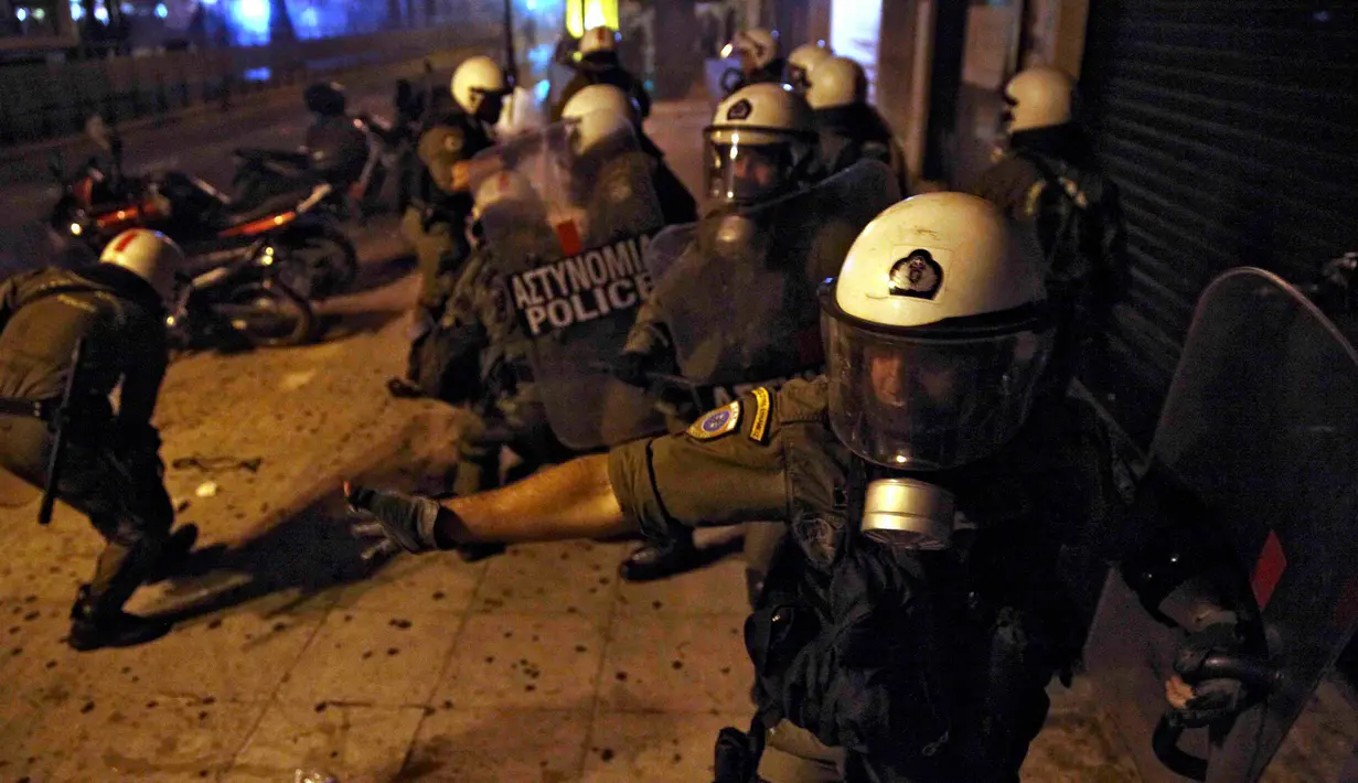Polisi anti huru hara berlindung dari proyektil yang pengunjuk rasa anti-bailout di Athena, Yunani, Rabu (15/7/2015). Unjuk rasa ini dilakukan menjelang pemungutan suara kesepakatan bailout. (REUTERS /Yiannis Kourtoglou)