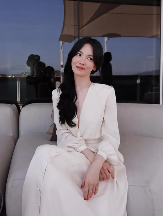 Di balik suasana santai tersebut, Song Hye Kyo juga tampak menjalani sesi pemotretan untuk Guerlain. Sebagai global ambassador rumah kecantikan asal Prancis tersebut, ia tampil anggun dalam gaun panjang berwarna ivory dengan potongan V-neck yang feminin. Siluet flowy dan detail kancing pada bagian depan menciptakan kesan romantis sekaligus elegan. [Dok/@kyo1122].