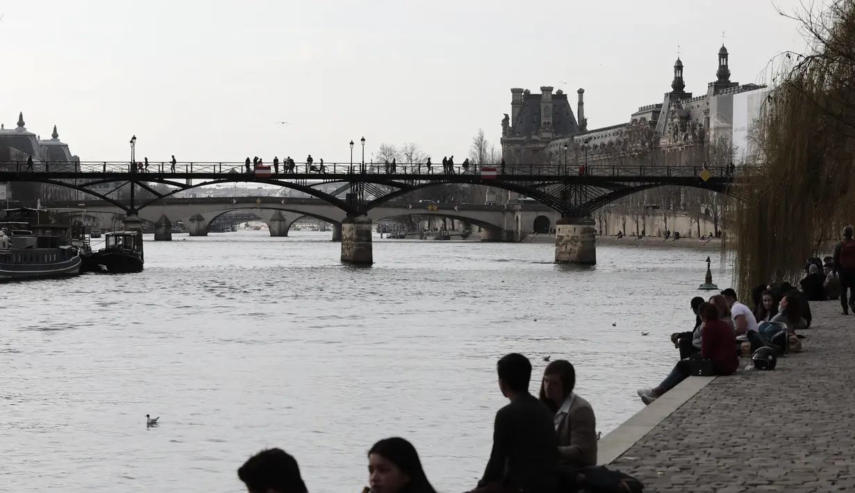 Orang-orang duduk di tepi sungai Seine di Paris, Rabu (3/3/2021).  Tingkat infeksi COVID-19 tetap tinggi selama beberapa minggu, dan pasien virus menempati 70% unit perawatan intensif negara itu. (AP Photo/Lewis Joly)