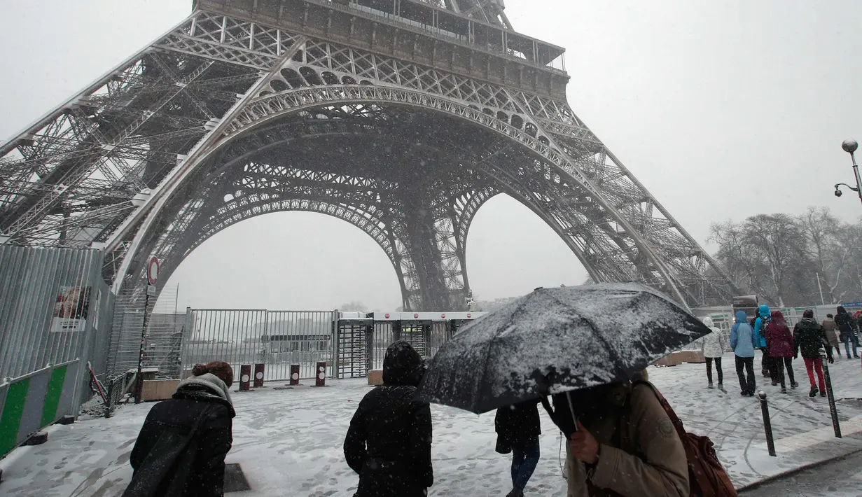 Pejalan kaki berjalan di dekat Menara Eiffel saat turun salju di Paris, Prancis, (6/2). Badan cuaca nasional Prancis Meteo France mengatakan sekitar setengah negara di eropa siaga atas bahaya tingkat salju dan es yang berbahaya. (AP Photo / Francois Mori)