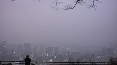 Seorang pria melihat ke arah gedung-gedung yang diselimuti kabut saat ia mengunjungi Menara Namsan pada hari yang tercemar di Seoul, Korea Selatan, Rabu (15/12/2021). (AFP/Anthony Wallace)