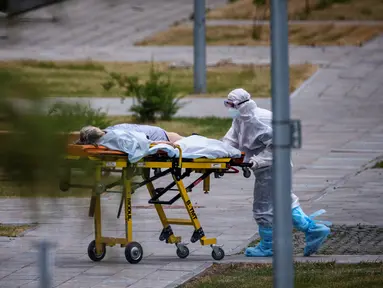 Petugas medis mengantar seorang perempuan menuju rumah sakit untuk pasien COVID-19 di pemukiman Kommunarka di luar Moskow, Rabu (30/6/2021). Rusia pada hari Rabu kembali melaporkan rekor kematian harian akibat virus Corona, dengan mencatat 669 kematian dalam 24 jam terakhir. (Dimitar DILKOFF/AFP)