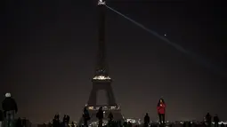 Sejumlah pengunjung berkumpul di dekat Menara Eiffel yang mengalami pemadaman sementara di Paris, Rabu (14/12). Pemadaman lampu Menara Eiffel ini sebagai simbol keprihatinan terhadap korban di Aleppo, Suriah. (AFP PHOTO/PHILIPPE LOPEZ)