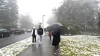 Orang-orang berjalan di sepanjang jalan selama hujan salju pertama musim ini di Katoomba di pegunungan Blue Mountains (10/6/2021). Suasana udara yang sejuk dan bersalju di Blue Mountains ketika musim dingin menjadi daya tarik wisatawan lokal di Sydney. (AFP/Saeed KHAN)