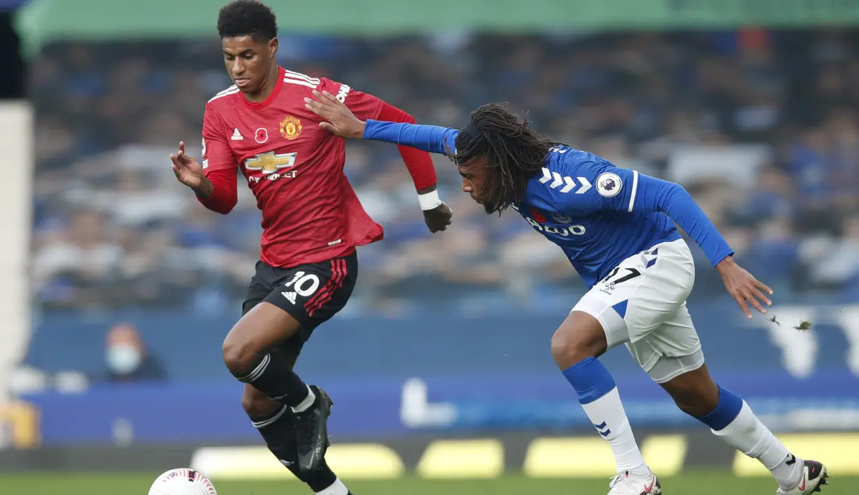 Penyerang Manchester United, Marcus Rashford, berebut bola dengan gelandang Everton, Alex Iwobi, pada laga lanjutan Liga Inggris di Goodison Park Stadium, Sabtu (7/11/2020) malam WIB. Manchester United menang 3-1 atas Everton. (Clive Brunskill/Pool via AP)