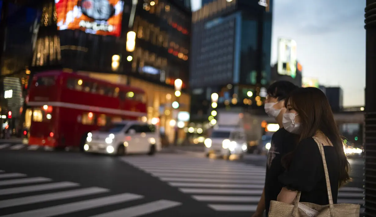Seorang pria dan seorang wanita menunggu lampu lalu lintas berubah di persimpangan di distrik perbelanjaan Ginza Tokyo, Kamis (23/9/2021). (AP Photo/Hiro Komae)