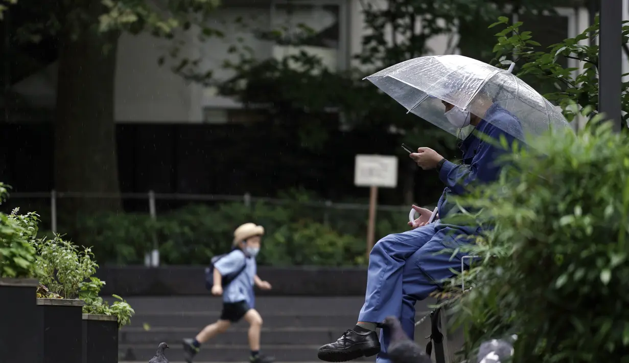 Seorang pria memakai masker melihat ponselnya di sebuah taman di Tokyo, Rabu, (23/9/2020). Badai tropis di Samudra Pasifik perlahan mendekati wilayah Tokyo pada hari Rabu, dan para pejabat mendesak penduduk berhati-hati dari perkiraan hujan lebat dan hembusan angin. (AP Photo/Eugene Hoshiko)