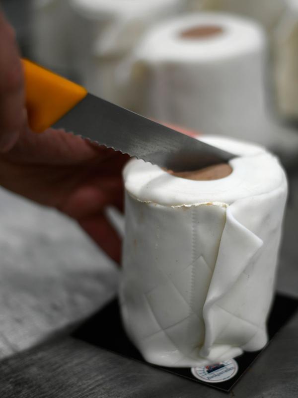 Seorang karyawan memotong kue berbentuk tisu toilet di toko roti Schuerener Backparadies di Dortmund, Jerman, 26 Maret 2020. Kelangkaan kertas tisu toilet memunculkan ide bagi pemilik toko roti itu, Tim Kortuem, membuat kue menyerupai barang yang diburu warga di tengah Covid-19. (Ina FASSBENDER/AFP