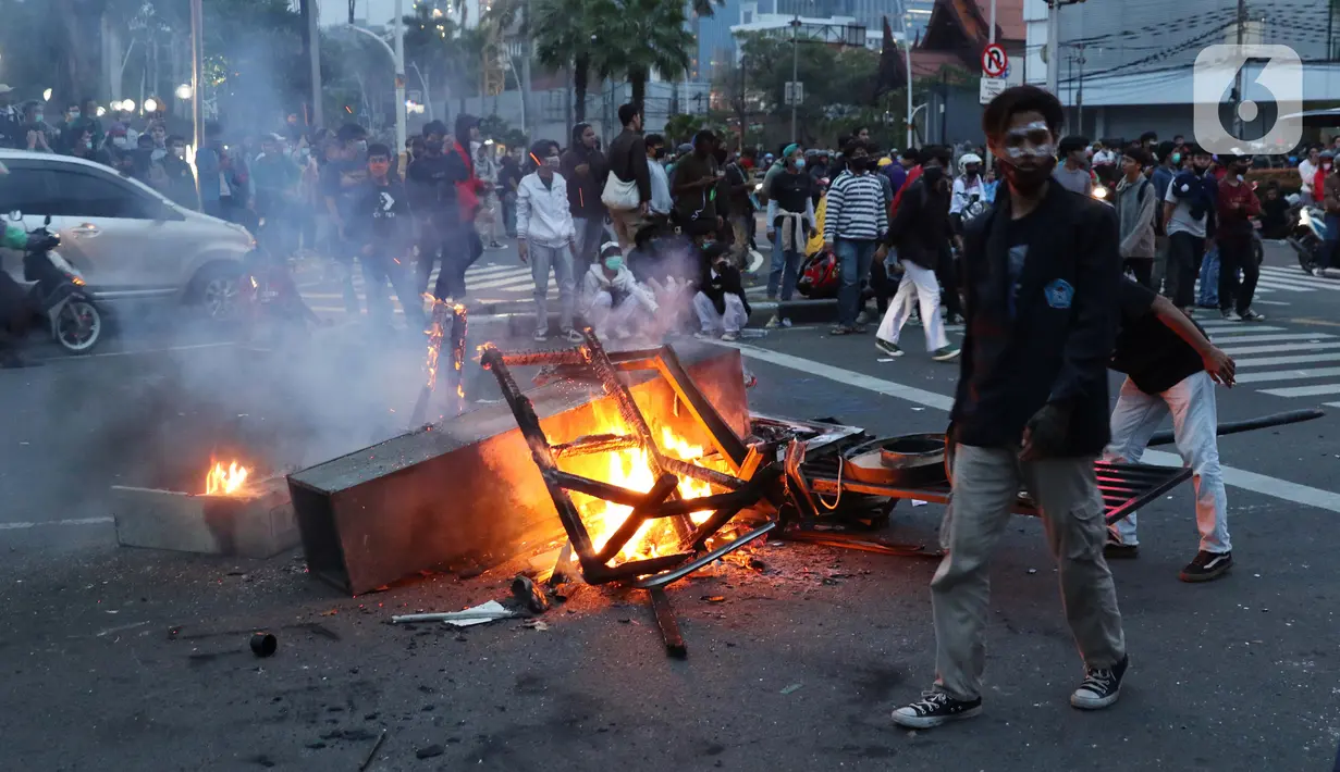 Seorang anak muda melintas di dekat kobaran api di kawasan Gondangdia, Jakarta, Kamis (8/10/2020). Aksi anarkis massa dilakukan saat berunjuk rasa menentang disahkan Omnibus Law UU Cipta Kerja. (Liputan6.com/Helmi Fithriansyah)