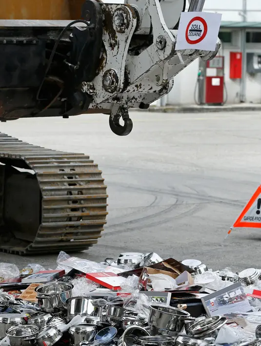 Sebuah alat berat bersiap menggilas panci palsu dan peralatan dapur yang disita Badan Bea Cukai Swiss di Jenewa, Swiss, Selasa (16/6/2015). (REUTERS/Pierre Albouy)