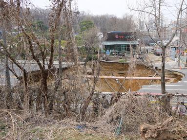 Seorang penyelidik mengambil foto lubang runtuhan di luar sebuah toko tanaman di sebuah jalan di Seoul, Korea Selatan pada tanggal 25 Maret 2025. (Anthony WALLACE/AFP)