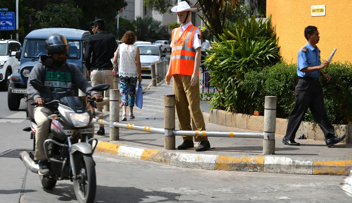 Pengendara melintasi manekin pria berseragam polisi lalu lintas di persimpangan jalan di Bangalore, India, Senin (16/12/2019). Dilengkapi dengan topi polisi, kemeja putih serta kacamata hitam, polisi manekin  itu siap “bertugas” di perempatan jalan yang kerap macet. (Manjunath KIRAN / AFP)
