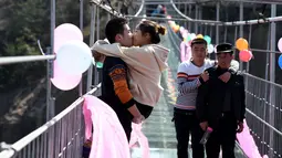 Dua orang pria memperhatikan kontestan yang sedang berciuman diatas sebuah jembatan kaca di Pingjiang, Provinsi Hunan, China (14/2). Kontes ini digelar untuk merayakan hari valentine yang jatuh pada setiap tanggal 14 Februari. (STR / AFP)