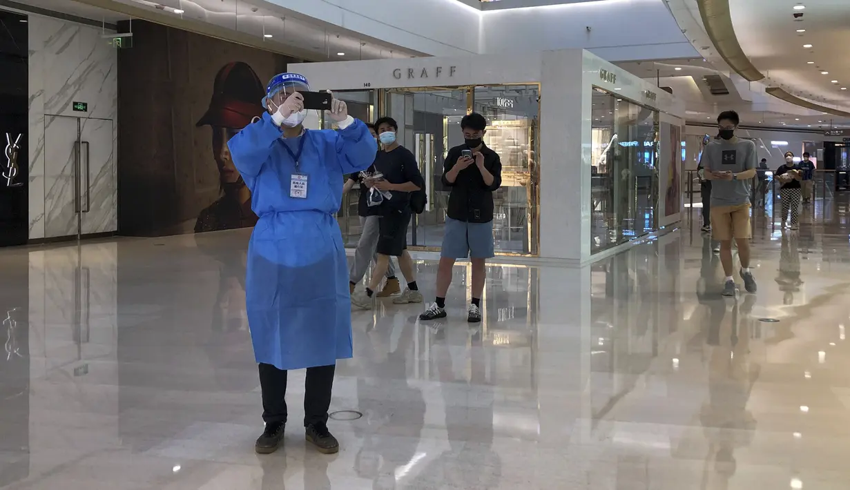 Seorang pekerja dengan pakaian pelindung mengambil gambar saat pembeli berjalan melalui pusat perbelanjaan yang dibuka kembali di Shanghai, Cina, Minggu (29/5/2022). Pembukaan kembali sebagian toko dan kantor di Beijing disambut oleh penduduk yang lelah dan pemilik toko yang berjuang untuk hidup kembali normal. Ditambah dengan pelonggaran pembatasan secara bertahap di Shanghai, itu menandakan bahwa yang terburuk telah berakhir dalam wabah kembar di kota-kota paling terkemuka di China. (AP Photo/Chen Si)