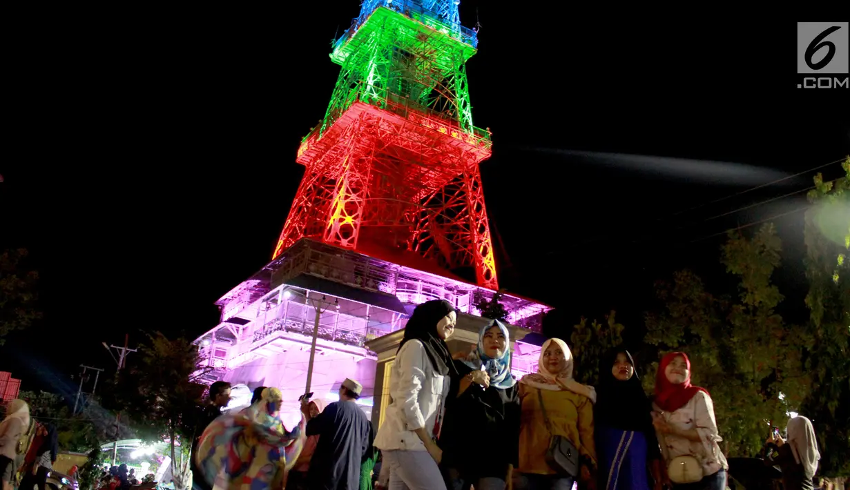 Warga berfoto dekat Pakaya Tower di kawasan taman Limboto, Kabupaten Gorontalo, Sabtu (12/1). Pakaya Tower berdiri megah bak Menara Eiffel dengan tata lampu warna-warni. (Liputan6.com/Arfandi Ibrahim)