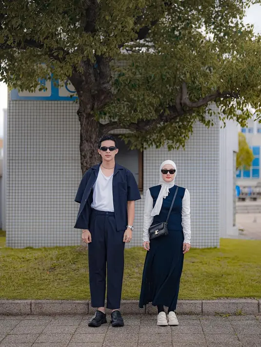 Manisnya penampilan pasutri Rey Mbayang dan Dinda Hauw di foto ini. Rey Mbayang tampil dengan kaus putih polos dengan padu padan top biru navy yang serasi dengan celana panjangnya. Sedangkan Dinda tampil cantik dengan manset putih yang ditumpuknya dengan dress panjang tanpa lengan berwarna biru navy dan hijab putih polos. [Foto: Instagram/rey_mbayang]