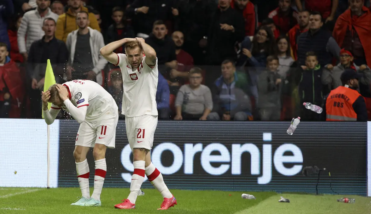Penyerang Polandia Karol Swiderski (kiri) memegangi kepalanya saat suporter melemparkan botol tak lama setelah mencetak gol ke gawang Albania pada lanjutan Kualifikasi Piala Dunia 2022, di Air Albania Stadium, Rabu (13/10/2021) dini hari WIB. Polandia mengalahkan Albania 1-0. (AP Photo/Franc Zhurda)