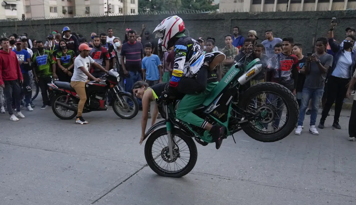 Pengendara sepeda motor dan penumpangnya melakukan wheelie di sepeda motornya selama pameran di lingkungan El Valle Caracas, Venezuela, Sabtu (31/7/2021). (AP Photo/Ariana Cubillos)