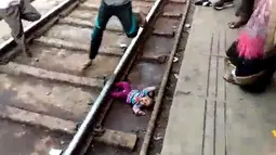 Gambar dari video pada 20 November 2018, bayi perempuan terjatuh dalam keadaan telentang di samping rel di stasiun kereta api di Mathura, Uttar Pradesh. Bayi satu tahun bernama Sahiba itu jatuh saat sebuah kereta melintas di atasnya. (NNIS / AFP)