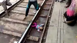 Gambar dari video pada 20 November 2018, bayi perempuan terjatuh dalam keadaan telentang di samping rel di stasiun kereta api di Mathura, Uttar Pradesh. Bayi satu tahun bernama Sahiba itu jatuh saat sebuah kereta melintas di atasnya. (NNIS / AFP)