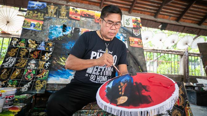 Seorang pengrajin melukis permukaan sebuah payung di Sentra Pembuatan Payung di Desa Bor Sang, Chiang Mai, Thailand, pada 1 November 2020. Desa Bor Sang, sekitar sembilan kilometer di sebelah timur Kota Tua Chiang Mai, terkenal sebagai daerah pembuat payung kertas. (Xinhua/Zhang Keren)