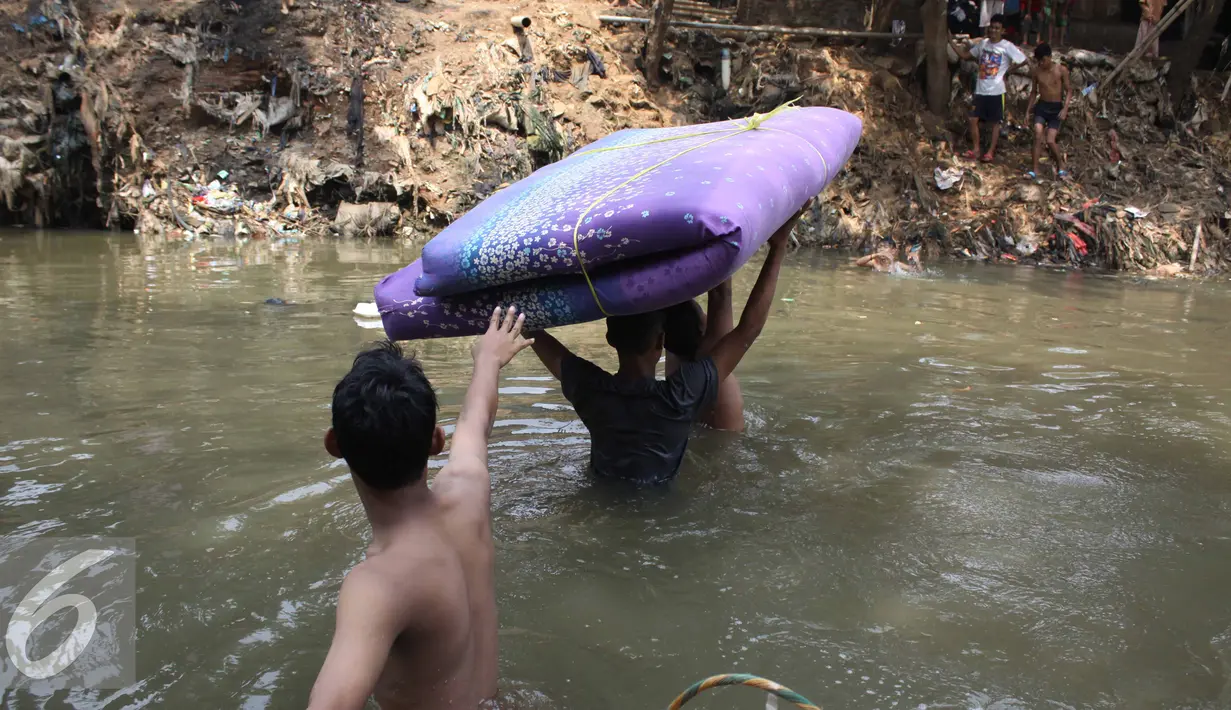 Sejumlah warga membawa kasur menyeberangi kali Ciliwung usai penggusuran di Kampung pulo, Jakarta, Jumat (21/8/2015). Penggusuran terkait rencana Pemprov DKI Jakarta yang akan melakukan normalisasi Kali Ciliwung. (Liputan6.com/Gempur Surya)