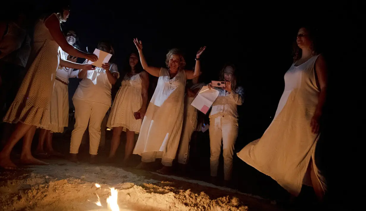 Wanita mengambil bagian dalam upacara Tashlich, di mana mereka menuliskan hal-hal yang ingin mereka lepaskan sebelum melemparkannya ke dalam api, di pantai di Tel Aviv, Israel (14/9/2021). (AP Photo/Maya Alleruzzo)