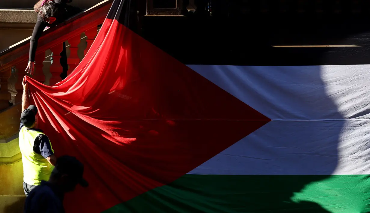 Para pengunjuk rasa menggantungkan bendera Palestina berukuran besar di dinding Balai Kota pada awal unjuk rasa menentang aksi militer Israel di Gaza saat mereka berkumpul di Sydney pada 9 Oktober 2023. (David GRAY/AFP)